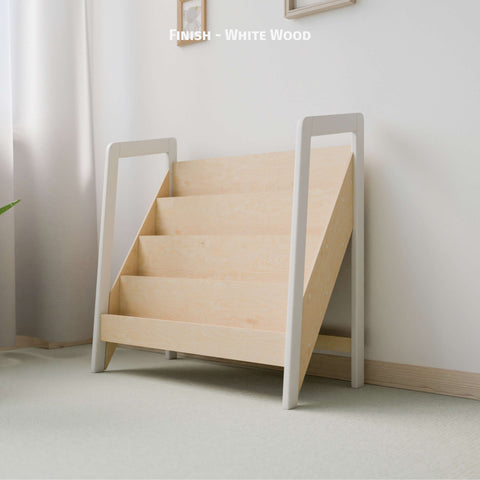 The image shows an empty Montessori-style bookshelf with a stylish finish combining white-painted wood on its sides and a natural wood finish for the shelves. This color scheme provides a clean and modern look, suitable for a contemporary nursery or child's play area. The shelf stands against a light-colored wall in a softly lit room, creating an inviting space for children's books or display items. The text on the image labels it as "Finish - White Wood," highlighting the dual-tone design.