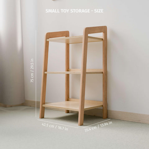 The image features an empty small Montessori-style toy storage shelf made of natural wood, with dimensions clearly labeled. The shelf stands 75 cm (29.5 inches) tall, 42.5 cm (16.7 inches) wide, and 35.4 cm (13.94 inches) deep. It has three tiers, providing ample storage space for organizing children's toys and items. The minimalist design is positioned against a light-colored wall in a softly lit room, promoting a clean and organized environment ideal for a child's play area or bedroom.