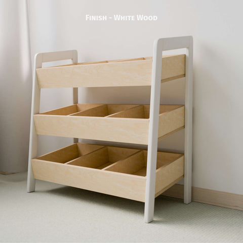 The image features an empty Montessori-style toy organizer with a white and natural wood finish. The organizer consists of three tiers of open bins made of natural wood, framed by white-painted sides. This minimalist design is ideal for organizing children's toys and books, promoting easy access and tidy habits. The piece is placed against a light-colored wall in a softly lit room, enhancing its clean and modern aesthetic.