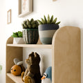 Detailed side view of a Montessori wall-mounted shelf, highlighting wooden craftsmanship and decorative items like plants and toys.